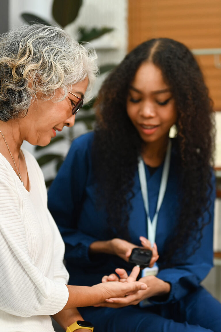 African nurse checking blood glucose levels of senior diabetic woman during a home visit. Diabetes and health care concept.