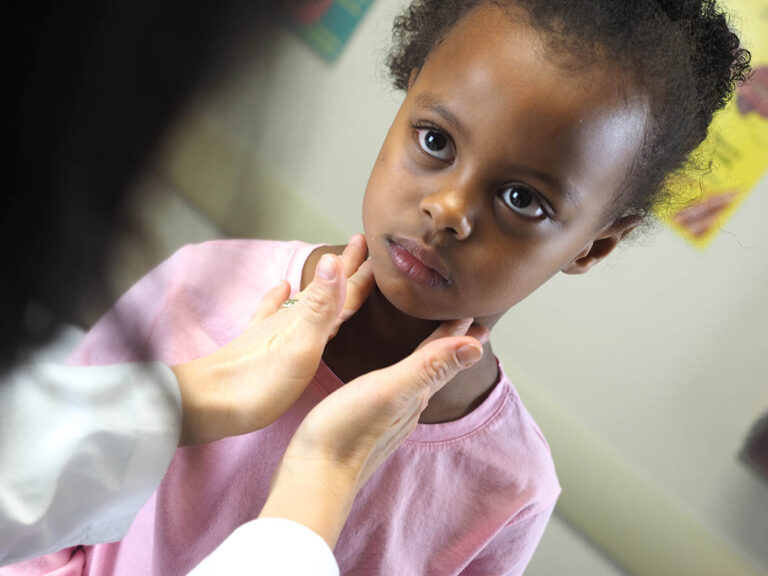 A doctor examining an African-American child's throat in a hospital